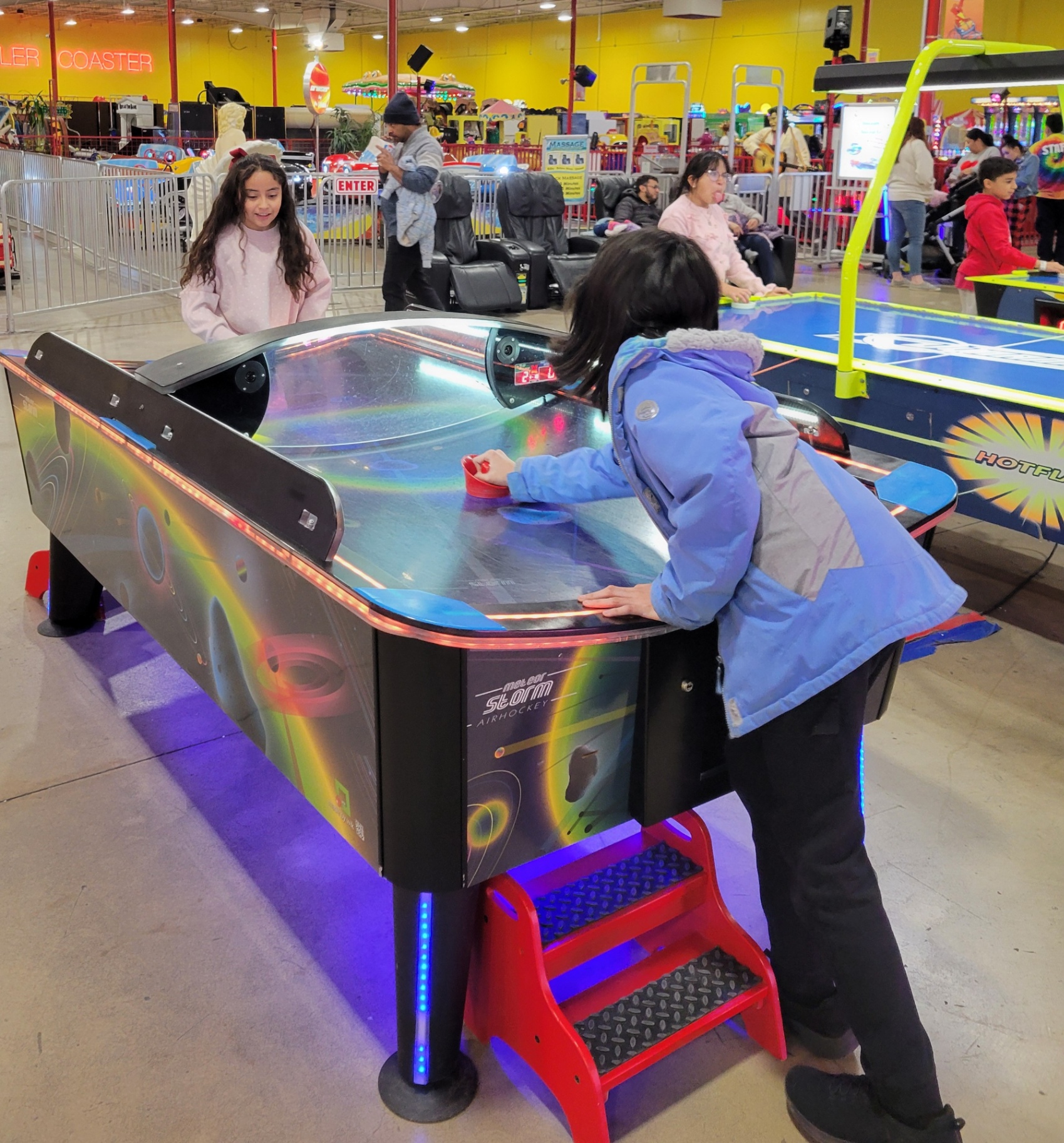 Two kids playing air hockey at a glowing table